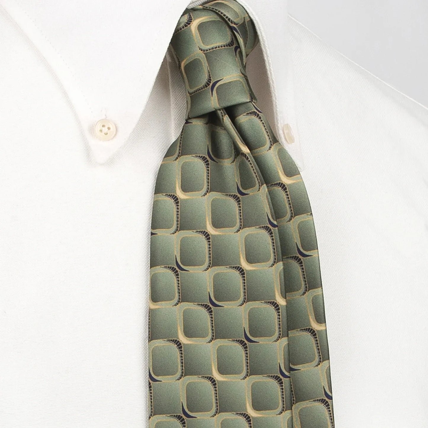 A gray-green men's necktie featuring a modern rounded square pattern with brown and black borders and gold accents is tied in a four-in-hand knot on a crisp white button-down shirt, suitable for business and professional settings.