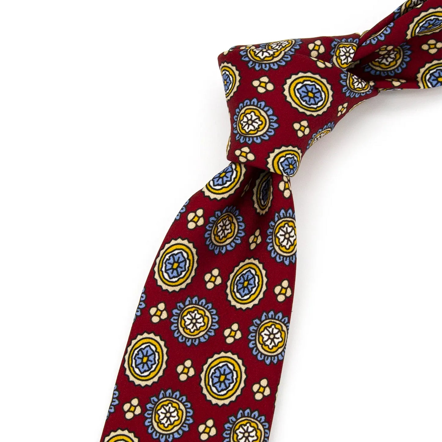 A neatly folded deep red men's necktie showcasing its cheerful pattern of circular floral designs in blue, yellow, and white, with small beige details, against a clean white surface.