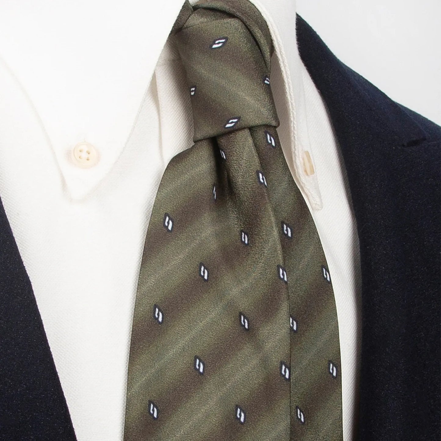A refined olive green men's necktie from XueDouLing Tie with a minimalist stripe and curve design in dark green and white is tied in a four-in-hand knot on a crisp white button-down shirt under a dark suit jacket, suitable for business and understated elegance.