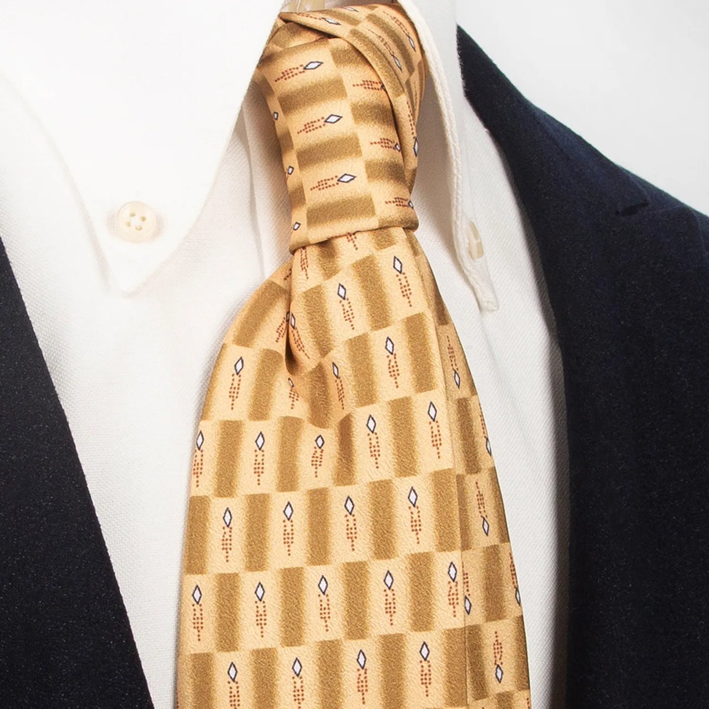 A gold and brown checkered men's necktie featuring an abstract geometric pattern in white, blue, and brown is tied in a four-in-hand knot on a crisp white button-down shirt, suitable for business and modern style.