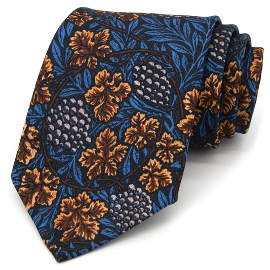 A neatly rolled dark blue men's necktie displaying its vintage vineyard pattern with brown leaves and light purple grapes against a clean white surface.