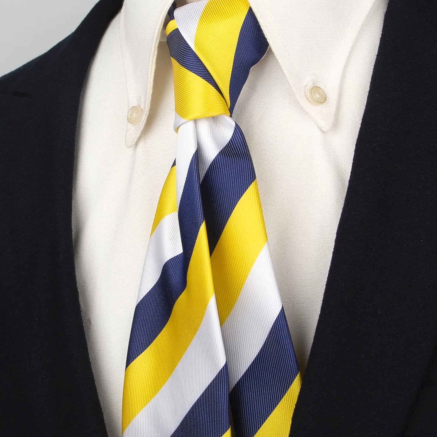 Close-up of a stylish navy blue, gold, and white striped silk tie worn with a classic white collared shirt and dark suit jacket, emphasizing its smart appearance.