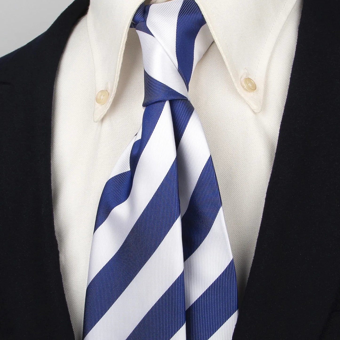 Close-up of a blue and white striped polyester tie worn with a classic white collared shirt and dark blazer, demonstrating its neat and polished look.
