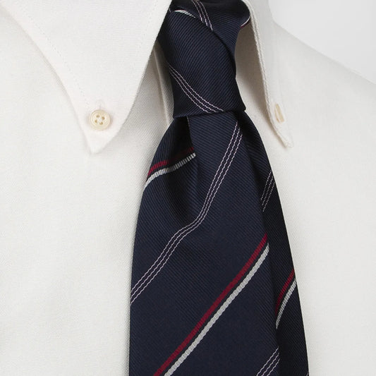 A close-up shows a dark blue men's necktie with thin red and white diagonal stripes tied in a Windsor knot on a white collared shirt. The knot is centered, and the collar's button is visible.