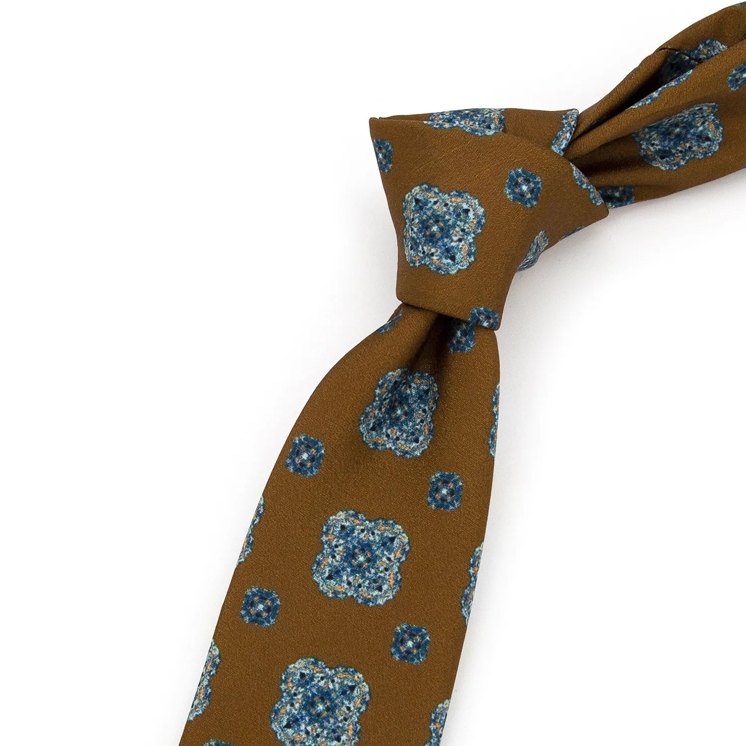 A brown men's necktie with a repeating blue and beige floral motif is partially tied, showcasing the pattern and texture against a white background.