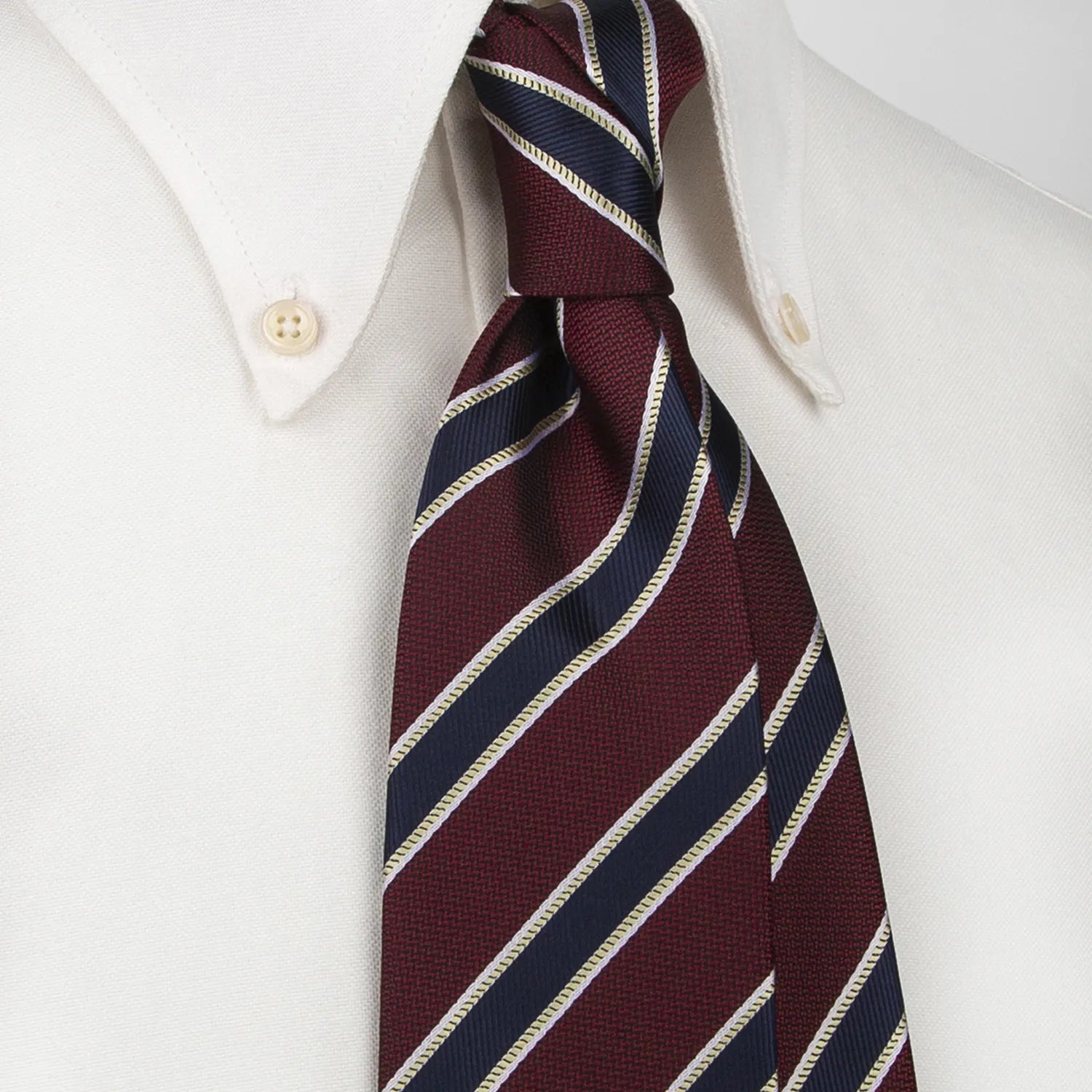 A tightly rolled burgundy men's necktie displaying diagonal stripes in navy blue and gold is set against a clean white backdrop.