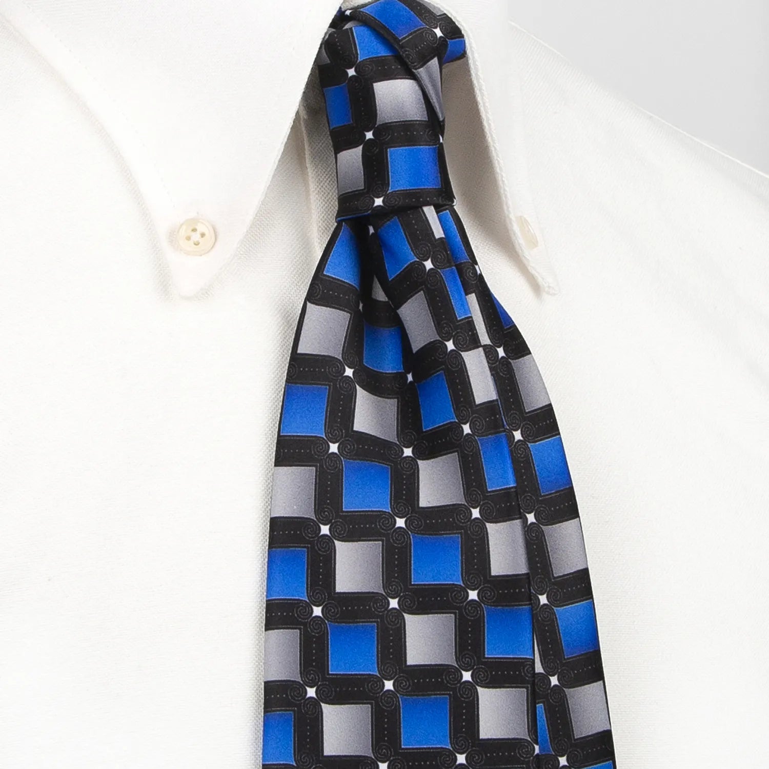 A black men's necktie with a dynamic geometric square pattern in blue and grey with white dot accents is neatly folded against a white background.