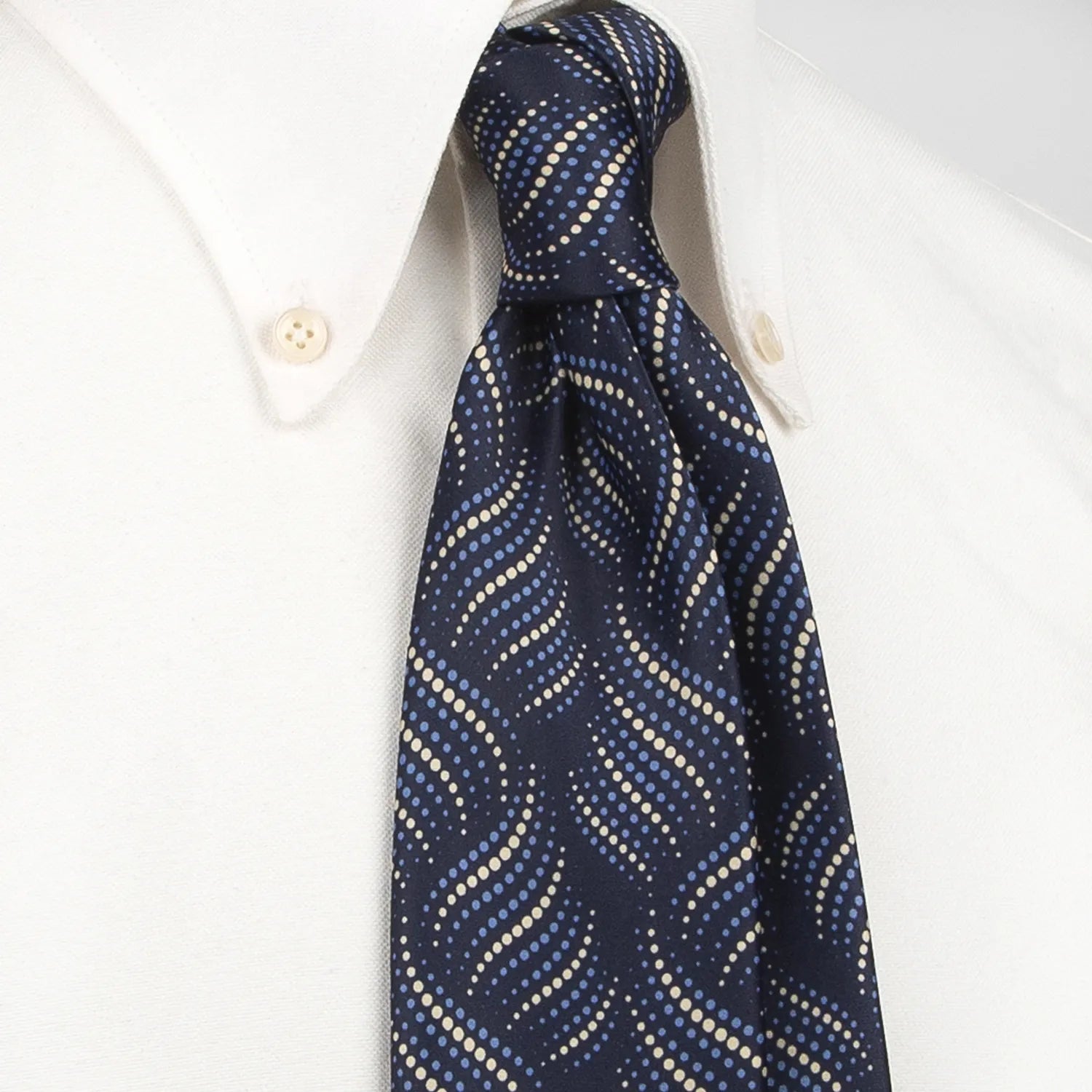 A neatly rolled dark blue men's necktie showcasing its modern wave-like pattern of light blue and beige dots against a clean white backdrop.