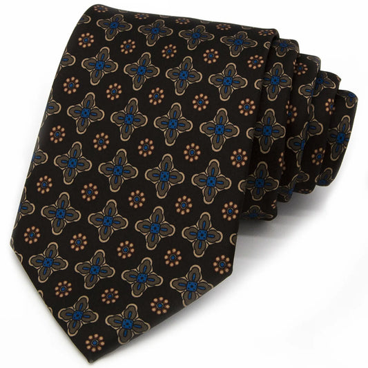 A dark brown men's necktie featuring a repeating pattern of small blue, beige, and brown floral and geometric elements is tied in a four-in-hand knot on a crisp white button-down shirt, suitable for business and professional settings.