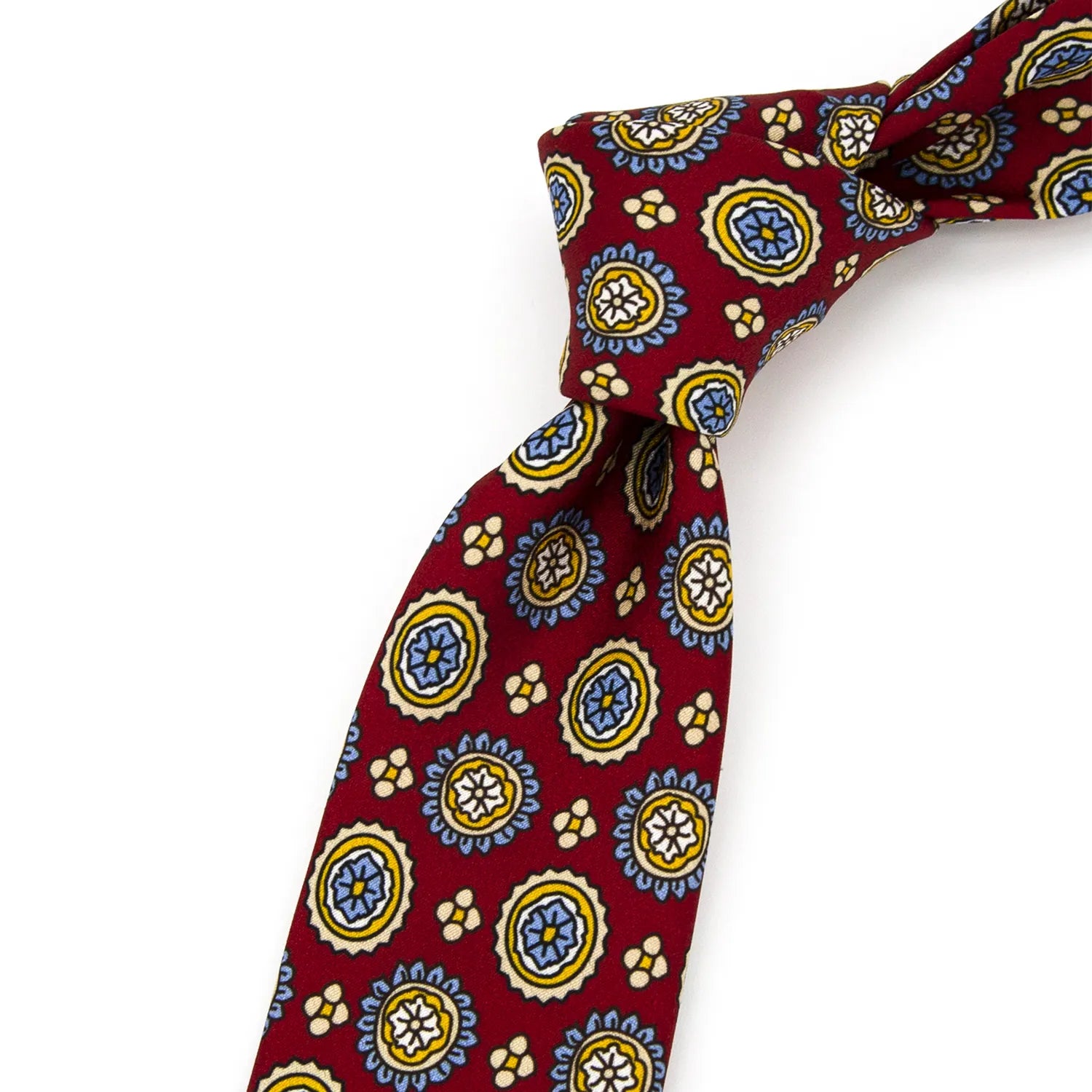 A neatly folded deep red men's necktie showcasing its cheerful pattern of circular floral designs in blue, yellow, and white, with small beige details, against a clean white surface.
