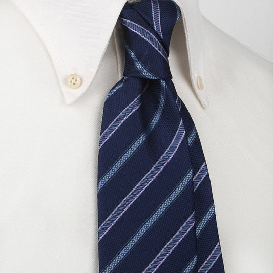 A dark blue men's necktie featuring diagonal stripes in light blue and pink with a subtle textured weave is tied in a four-in-hand knot on a crisp white button-down shirt, suitable for business and professional settings.