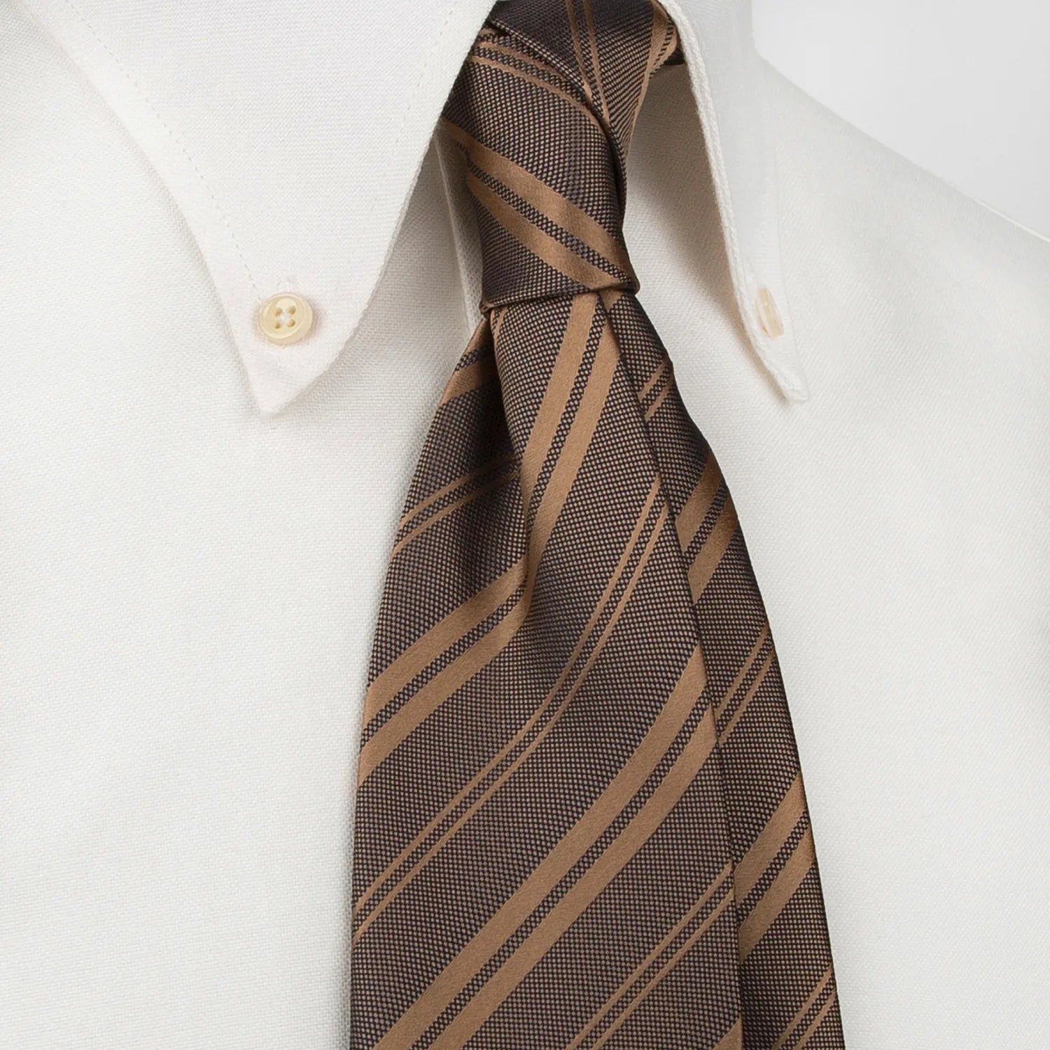 A dark brown men's necktie featuring diagonal stripes in a lighter brown hue, both with a subtle woven texture, is tied in a four-in-hand knot on a crisp white button-down shirt, suitable for business and professional settings.