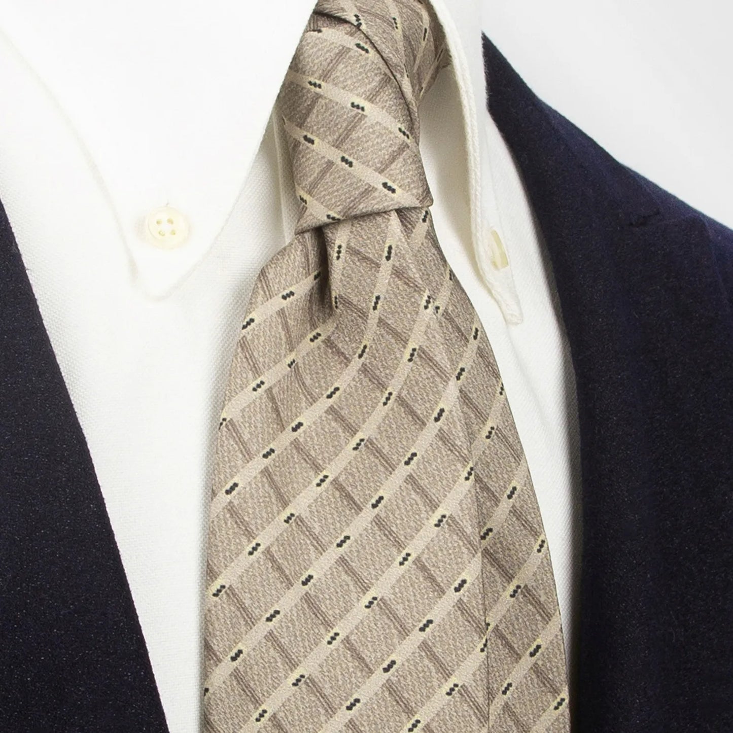 A refined light brown men's necktie from XueDouLing Tie with a minimalist geometric design of dark brown rhombuses and yellow accents is tied in a four-in-hand knot on a crisp white button-down shirt under a dark suit jacket, suitable for business and understated elegance