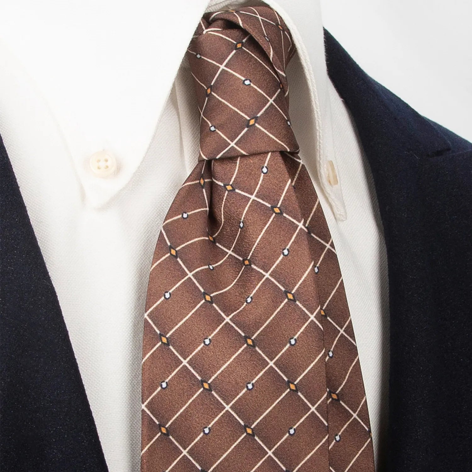 A stylish brown men's necktie from XueDouLing Tie showcasing its contemporary grid and dot design in white, orange, and light blue, tied in a four-in-hand knot on a crisp white button-down shirt under a dark blazer, suitable for business casual and modern events.