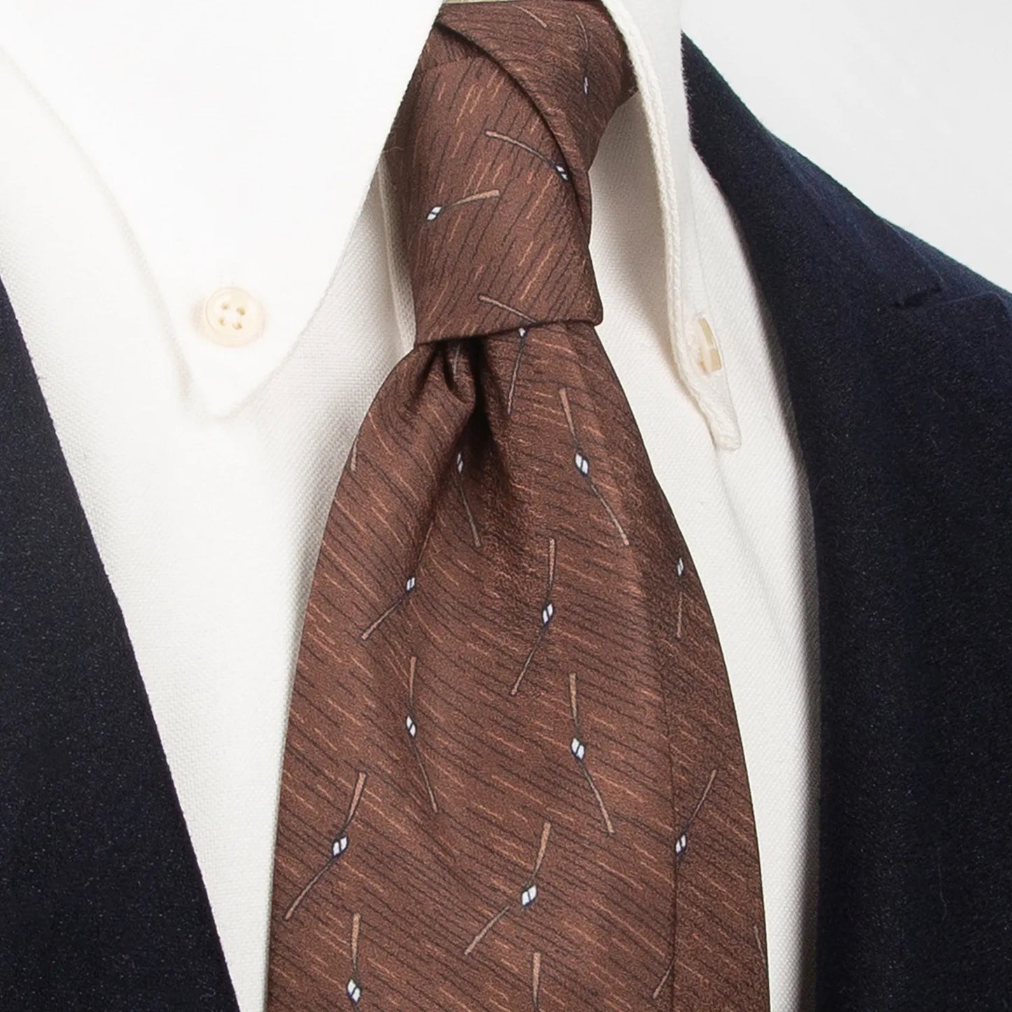 A stylish brown men's necktie from XueDouLing Tie showcasing its contemporary abstract line and diamond design in white, beige, and brown, tied in a four-in-hand knot on a crisp white button-down shirt under a dark blazer, suitable for business casual and modern events.