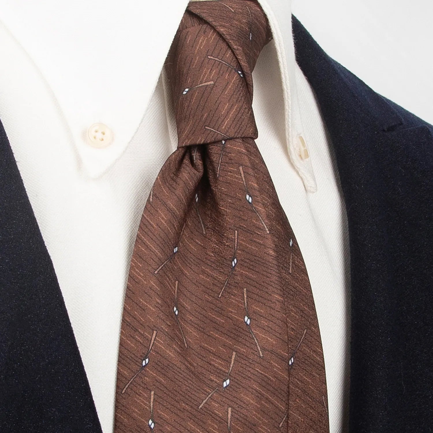 A stylish brown men's necktie from XueDouLing Tie showcasing its contemporary abstract line and diamond design in white, beige, and brown, tied in a four-in-hand knot on a crisp white button-down shirt under a dark blazer, suitable for business casual and modern events.