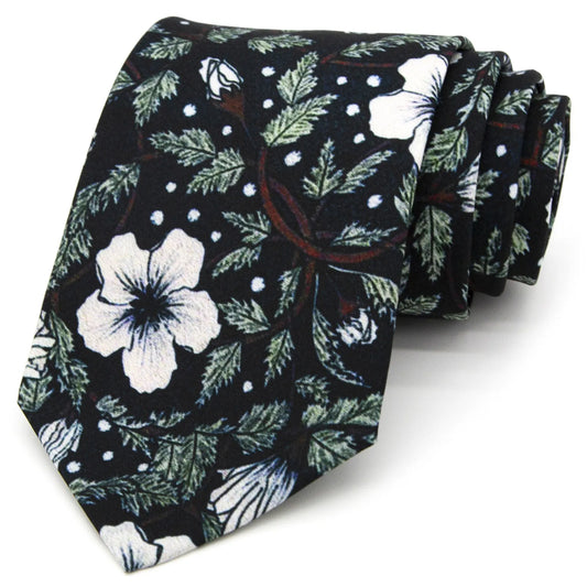 An elegant deep black men's necktie from XueDouLing Tie showcasing its delicate floral design with white flowers and green foliage, accented by small white dots, tied in a four-in-hand knot on a crisp white button-down shirt under a dark blazer, suitable for business casual and stylish events.