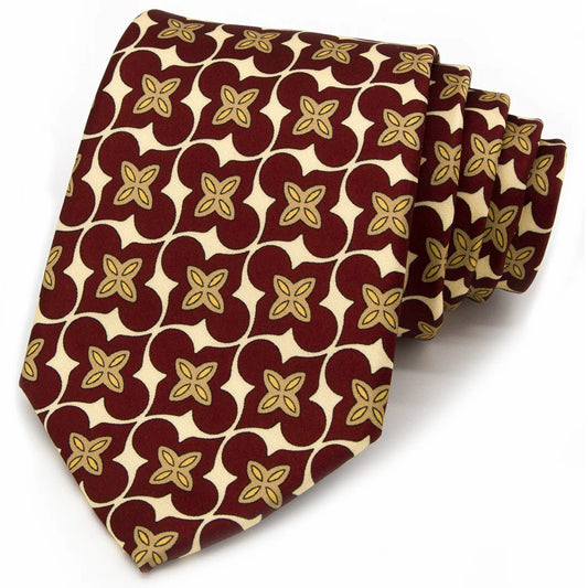 A neatly rolled deep red men's necktie showcasing its classic floral and curved geometric design in beige and gold against a clean white backdrop.