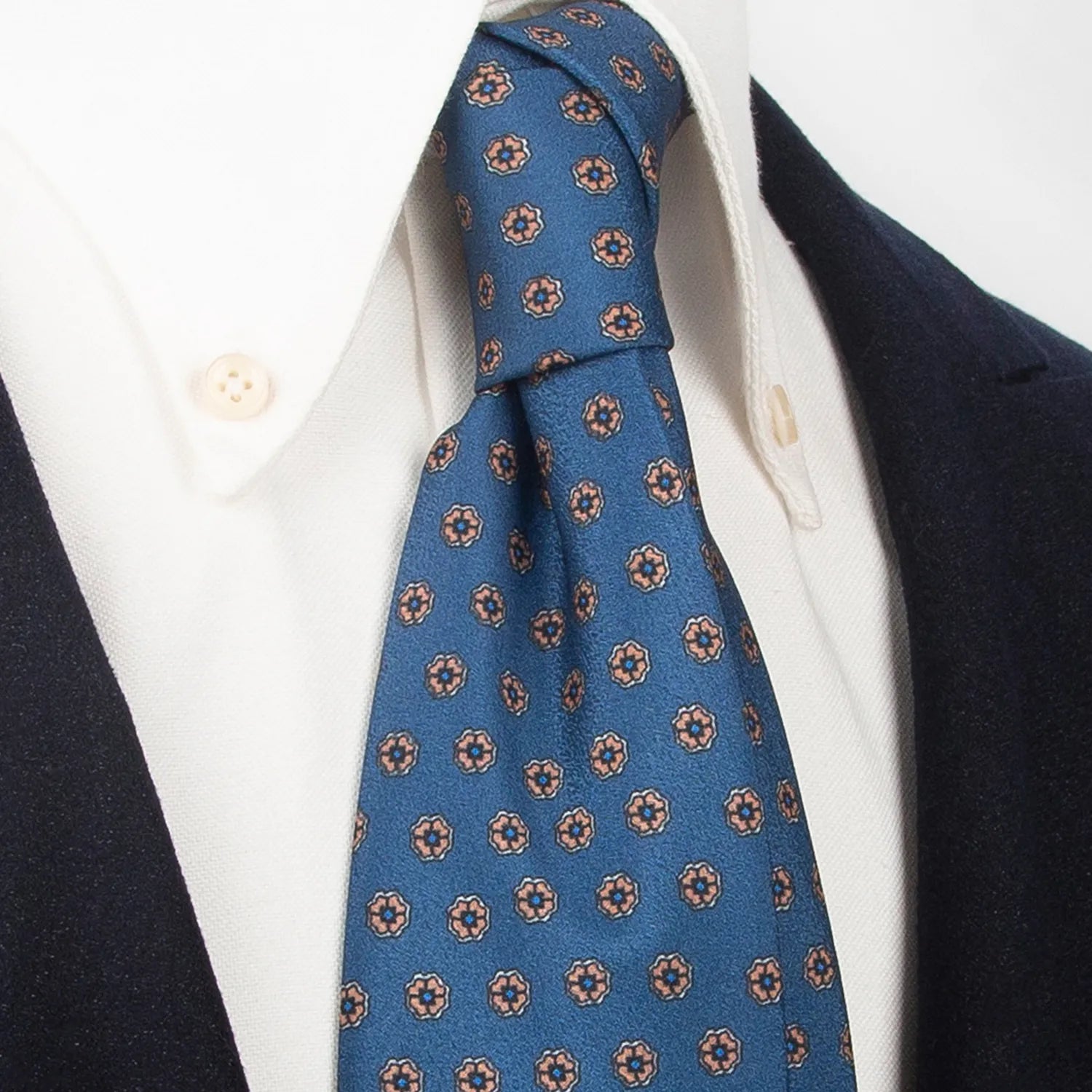 A neatly rolled blue men's necktie showcasing its subtle yet intricate pattern of small brown and beige floral dots against a clean white backdrop.
