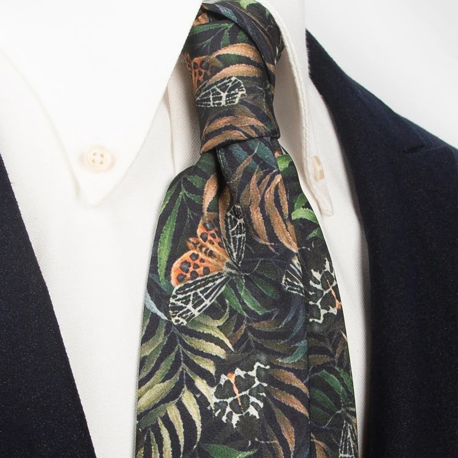 An artistic dark black men's necktie from XueDouLing Tie showcasing its distinctive butterfly and foliage design in brown, green, and beige, tied in a four-in-hand knot on a crisp white button-down shirt under a dark blazer, suitable for business casual and stylish events.