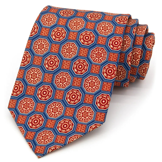 A neatly rolled blue men's necktie showcasing its ornate geometric floral design in red, beige, and brown against a clean white backdrop.