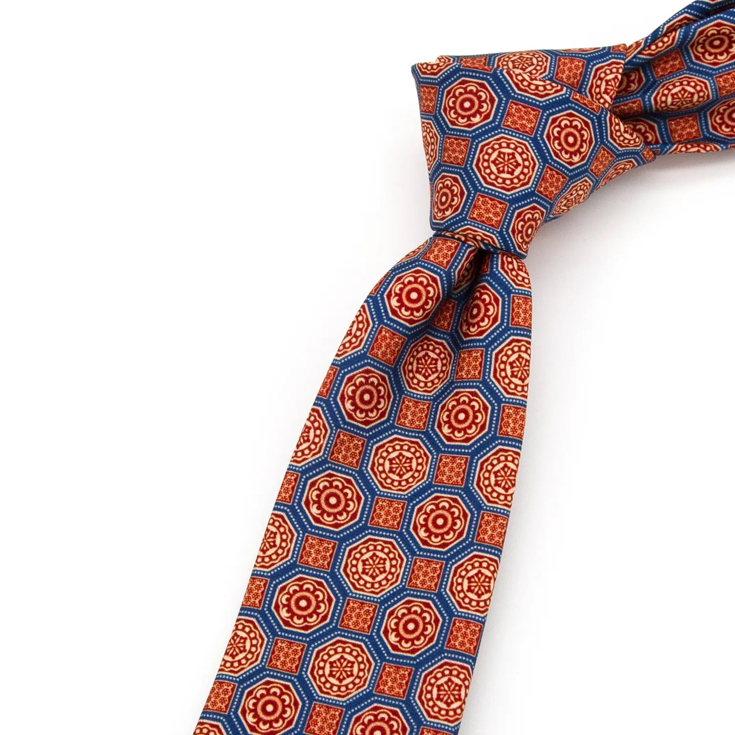 A blue men's necktie laid flat, displaying its intricate geometric floral pattern in red, beige, and brown.