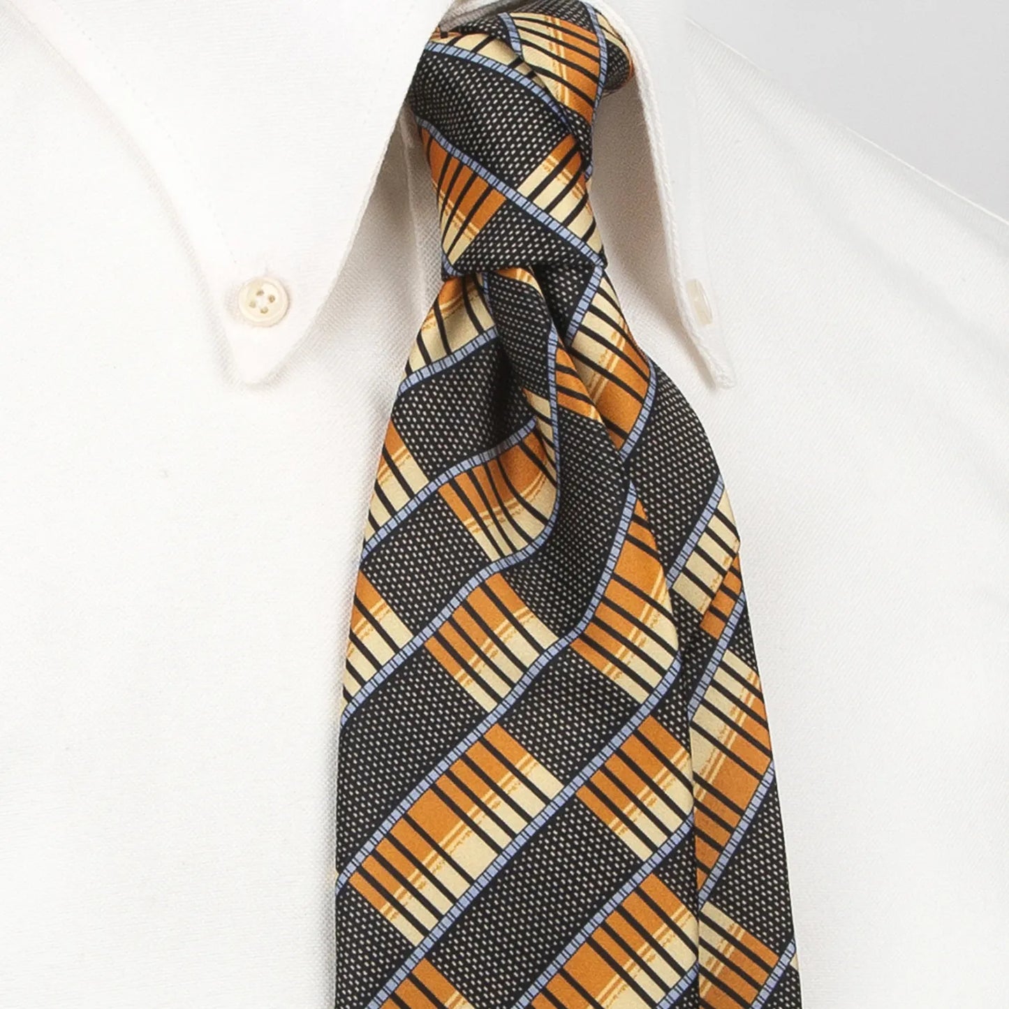 A dark grey men's necktie featuring a modern angled plaid pattern in orange, beige, and light blue with a subtle texture is tied in a four-in-hand knot on a crisp white button-down shirt, suitable for business and contemporary style.