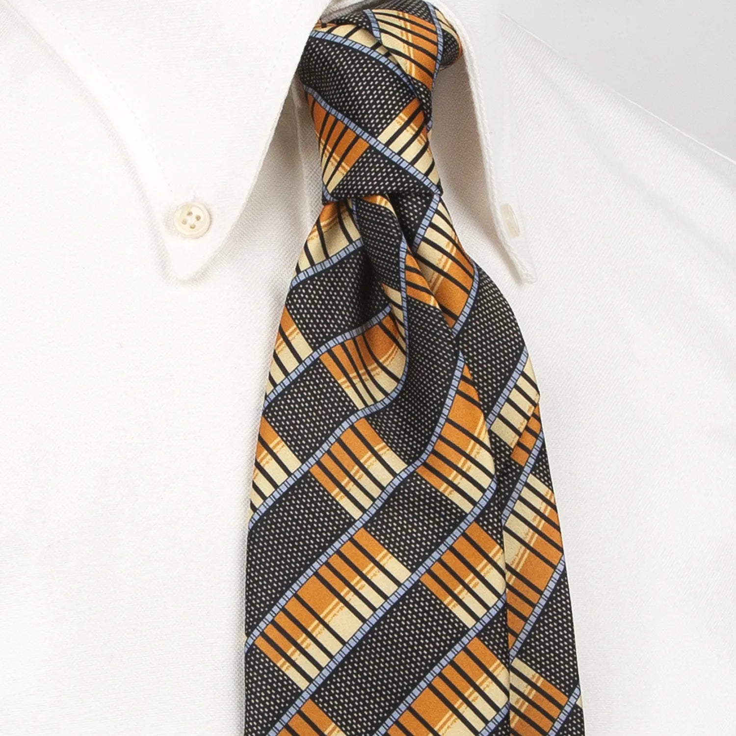 A dark grey men's necktie featuring a modern angled plaid pattern in orange, beige, and light blue with a subtle texture is tied in a four-in-hand knot on a crisp white button-down shirt, suitable for business and contemporary style.