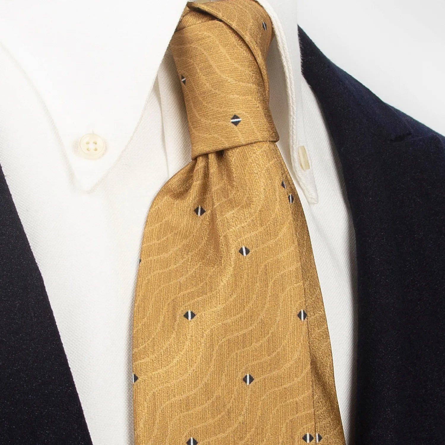 An elegant gold and brown men's necktie from XueDouLing Tie showcasing its contemporary wave and diamond design in beige, black, and white, tied in a four-in-hand knot on a crisp white button-down shirt under a dark blazer, suitable for business casual and modern style.