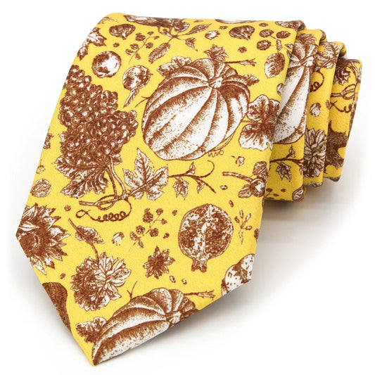 A bright yellow men's necktie featuring a festive autumn harvest pattern with pumpkins, grapes, and sunflowers in shades of brown and beige is casually knotted against a white background.