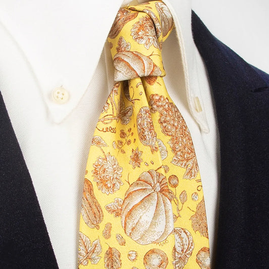 A vibrant yellow men's necktie from XueDouLing Tie showcasing its unique fall harvest design with pumpkins, grapes, and sunflowers in brown and beige, tied in a four-in-hand knot on a crisp white button-down shirt under a dark blazer, suitable for casual and holiday events.