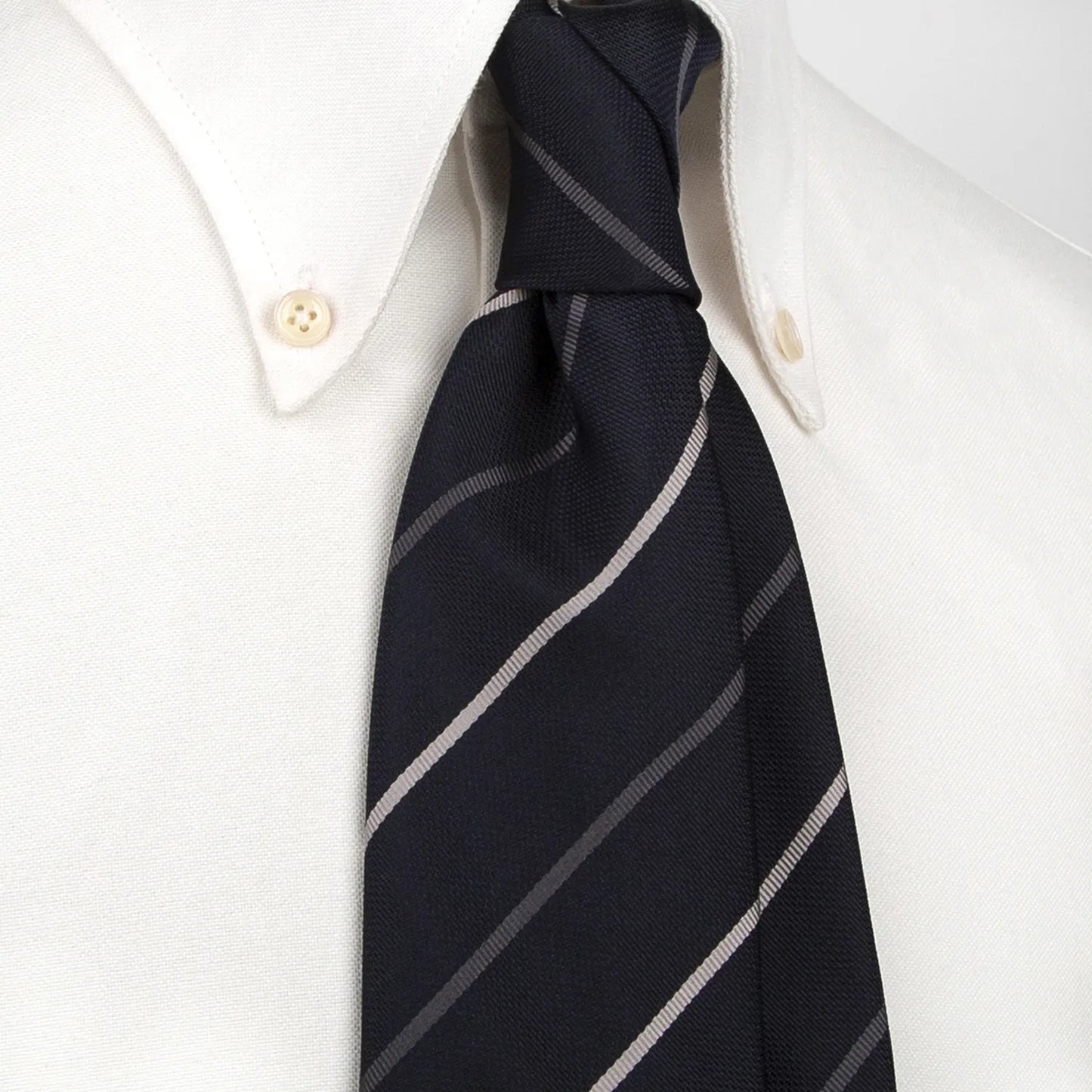 A neatly rolled deep blue men's necktie showcasing its diagonal stripe pattern in white and grey against a clean white surface.