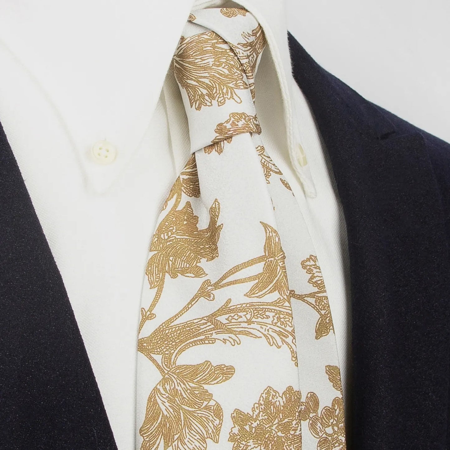 An elegant light off-white men's necktie from XueDouLing Tie showcasing its delicate botanical print with brown flowers and leaves, tied in a four-in-hand knot on a crisp white button-down shirt under a dark blazer, suitable for business casual and graceful events.