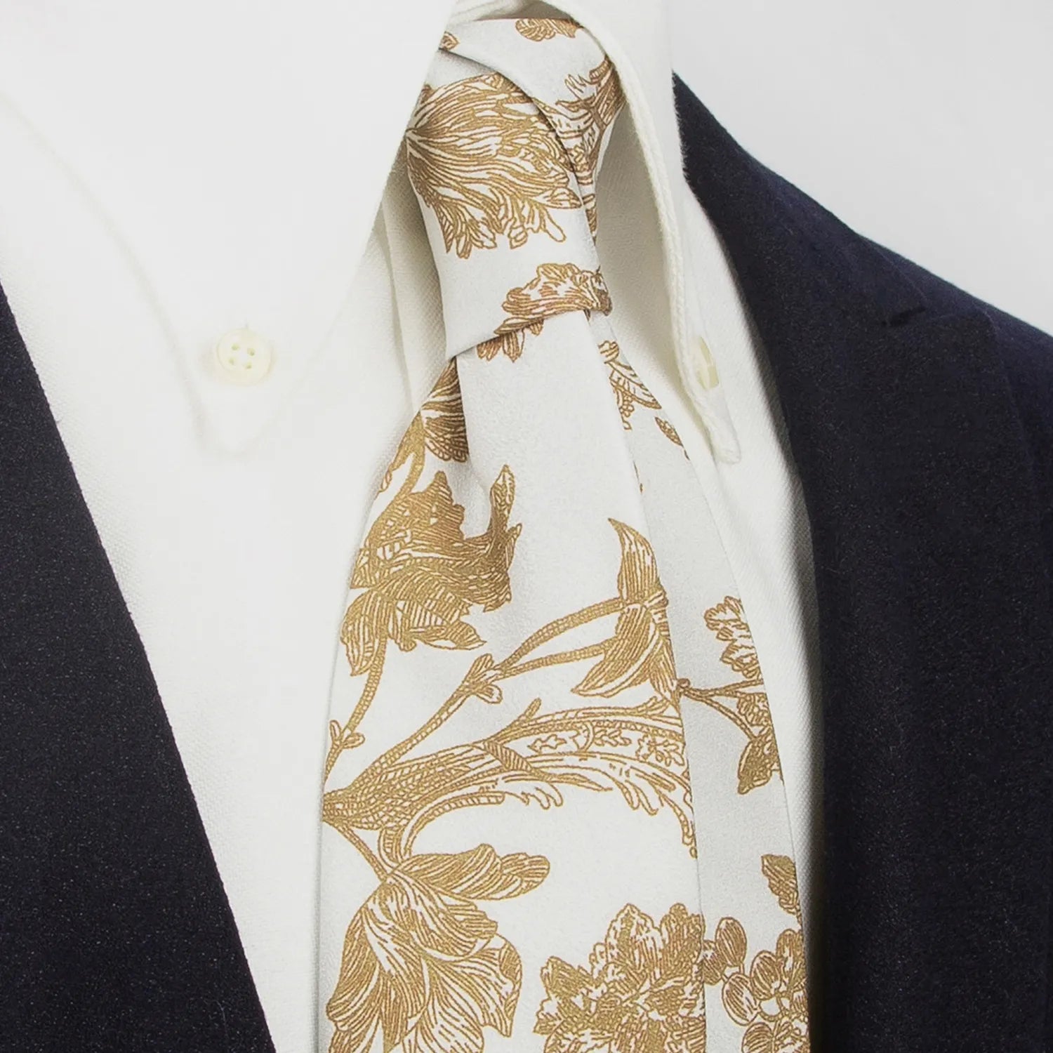 An elegant light off-white men's necktie from XueDouLing Tie showcasing its delicate botanical print with brown flowers and leaves, tied in a four-in-hand knot on a crisp white button-down shirt under a dark blazer, suitable for business casual and graceful events.