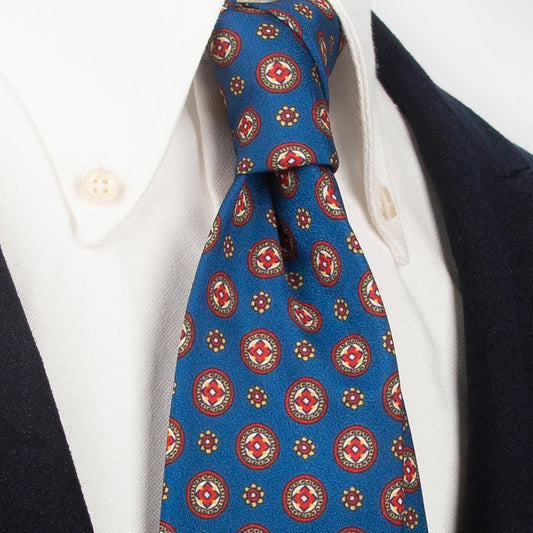 A striking azure men's necktie from XueDouLing Tie showcasing its dynamic geometric and floral design in red, white, and yellow, tied in a four-in-hand knot on a crisp white button-down shirt under a dark blazer, suitable for business casual and stylish events.