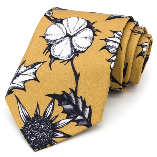 A mustard yellow men's necktie featuring a unique botanical pattern with black and white thistle and cotton plant illustrations is casually knotted against a white background.