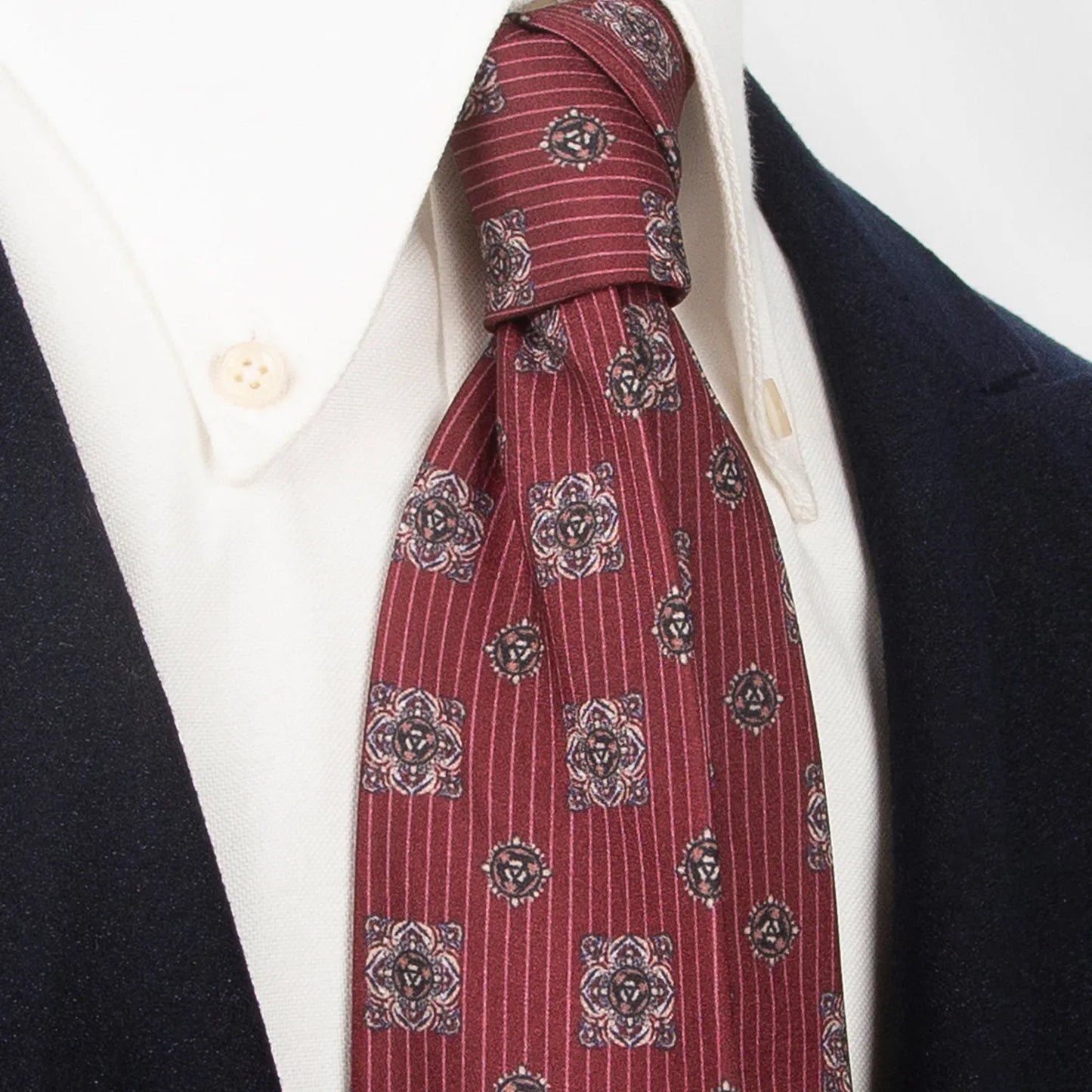 A rolled-up rich wine red men's necktie with white polka dots, displaying the full pattern and quality of the fabric against a white background, ready for storage or travel.