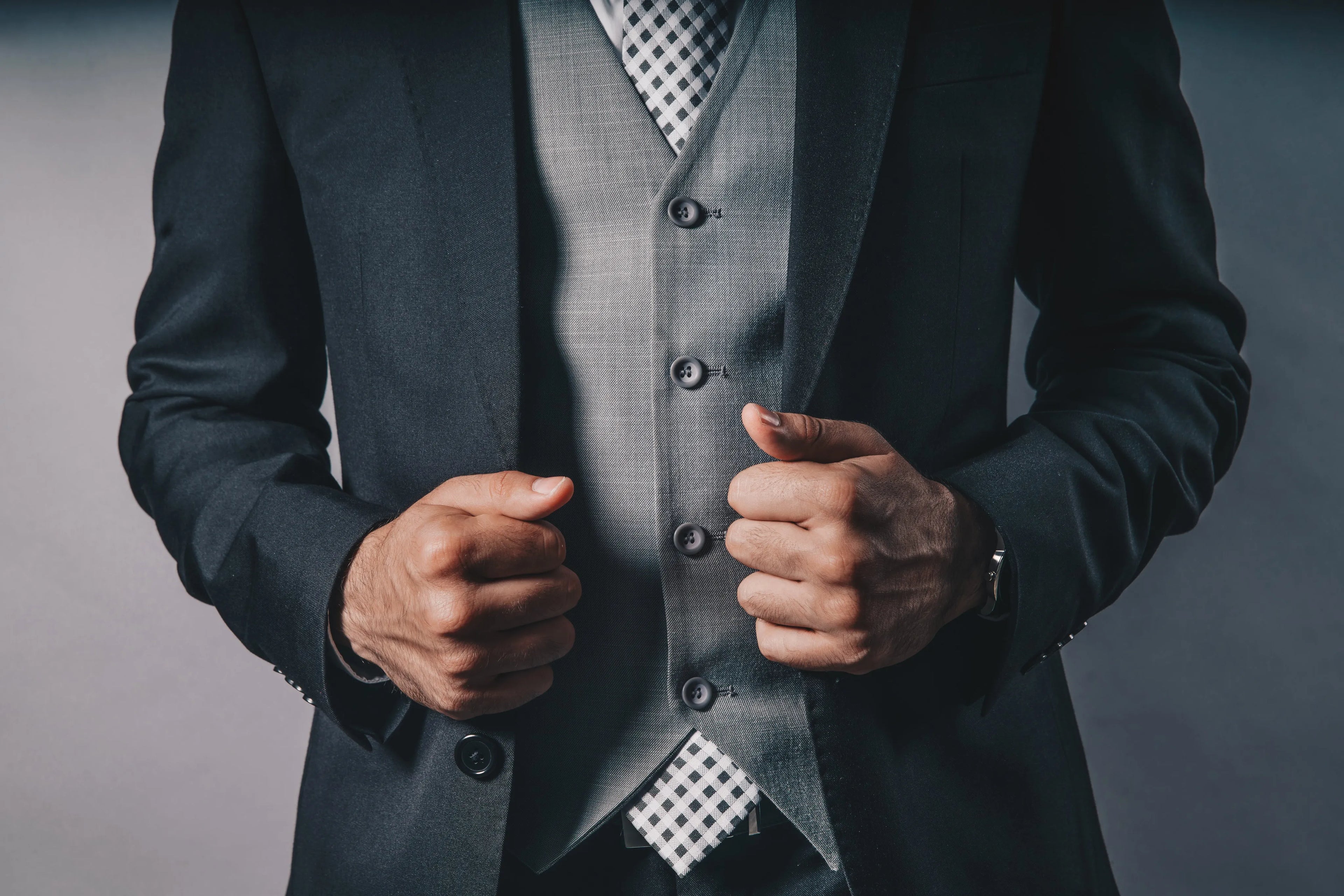 Close-up of a person wearing a dark suit with a gray vest and patterned tie.