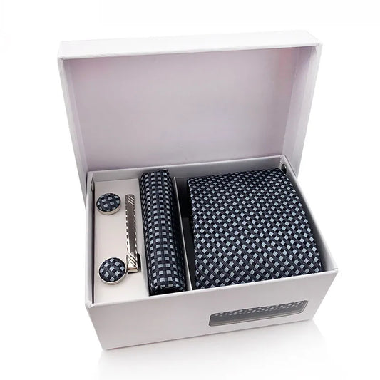 A complete men's tie set laid out, featuring a deep navy blue necktie with a subtle white and red small checkered pattern, a matching pocket square, and a pair of silver-toned cufflinks, ready for a formal or business occasion.