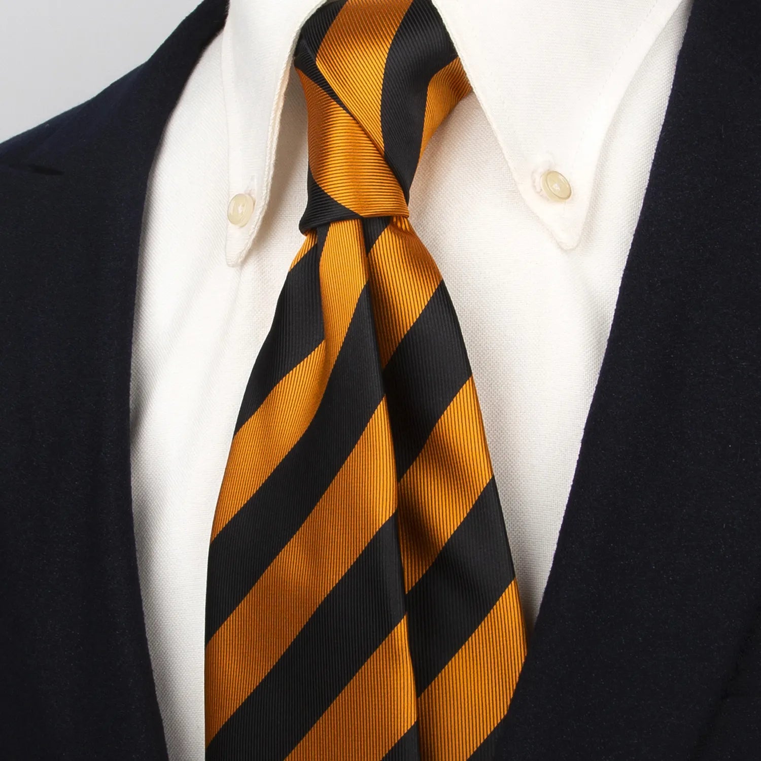 Black and gold striped silk tie worn with a white button-down shirt and a dark blazer, highlighting its sophisticated appearance when styled.