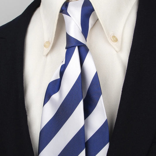 Close-up of a blue and white striped polyester tie worn with a classic white collared shirt and dark blazer, demonstrating its neat and polished look.
