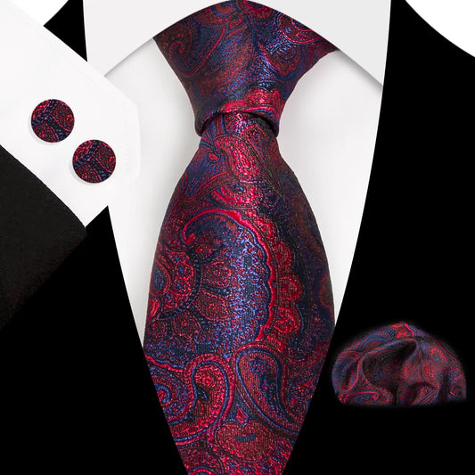 A close-up shot of a richly patterned polyester tie in a deep red and navy paisley design, worn with a white shirt and black suit, accompanied by a matching pocket square and cufflinks.