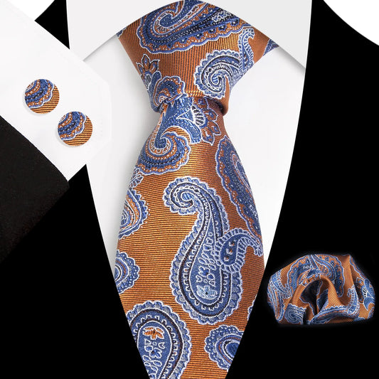 A coordinated set featuring a rolled rust orange and blue paisley polyester tie, a folded matching pocket square, and two round cufflinks, all displaying an intricate pattern on a white background.