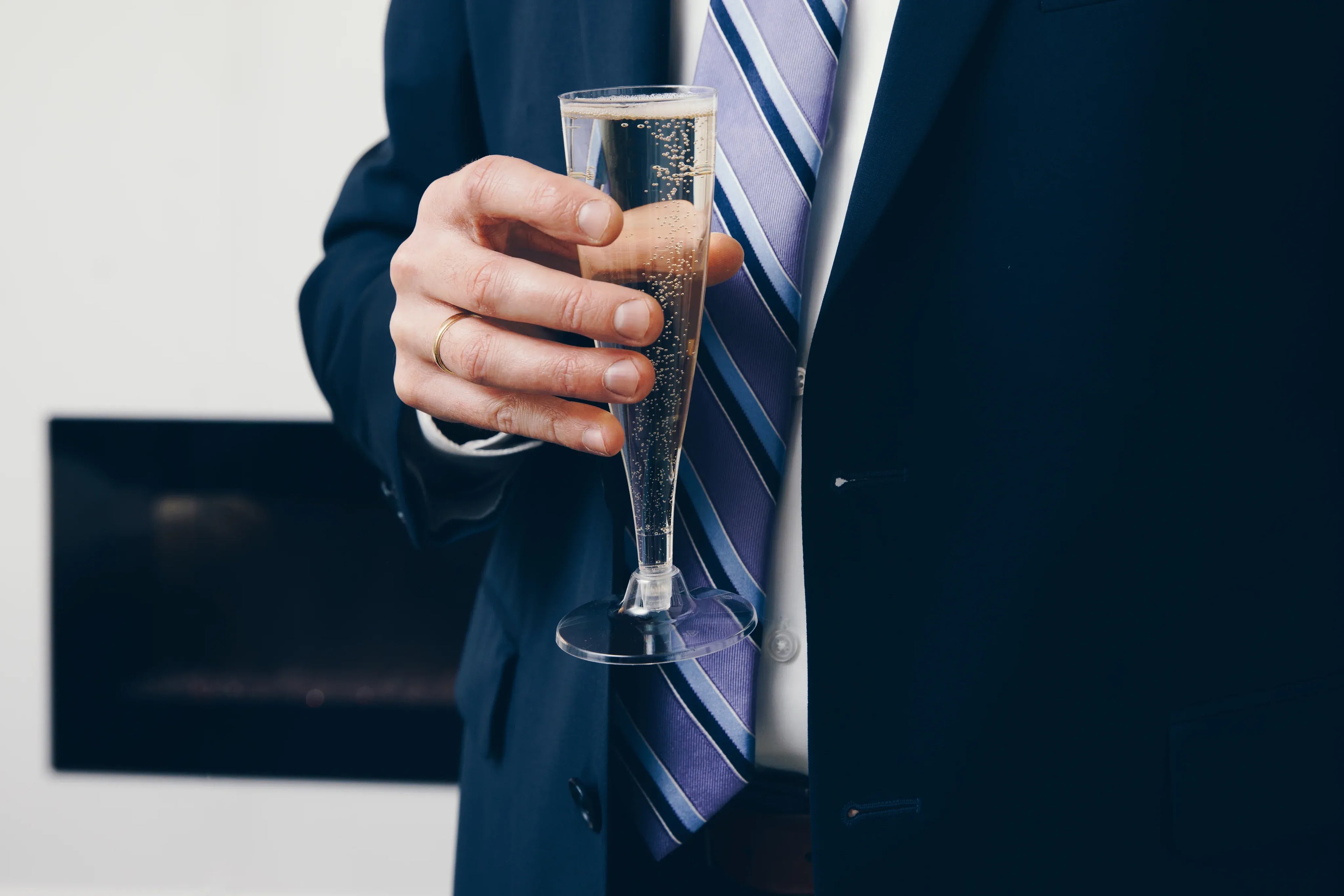 Person in suit holding a glass of champagne.