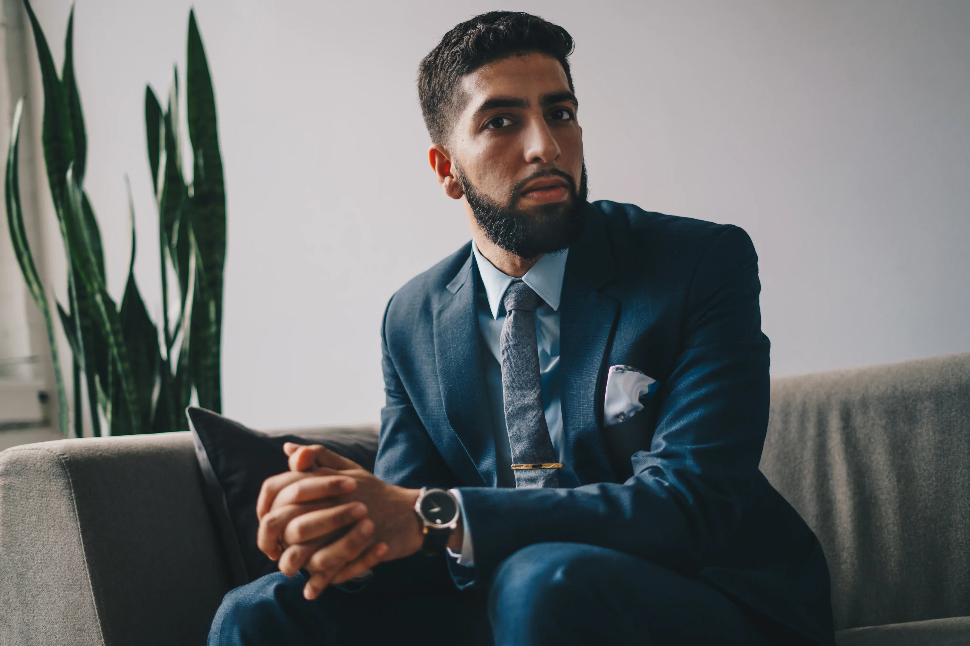 Man in a suit sitting on a couch with a plant in the background