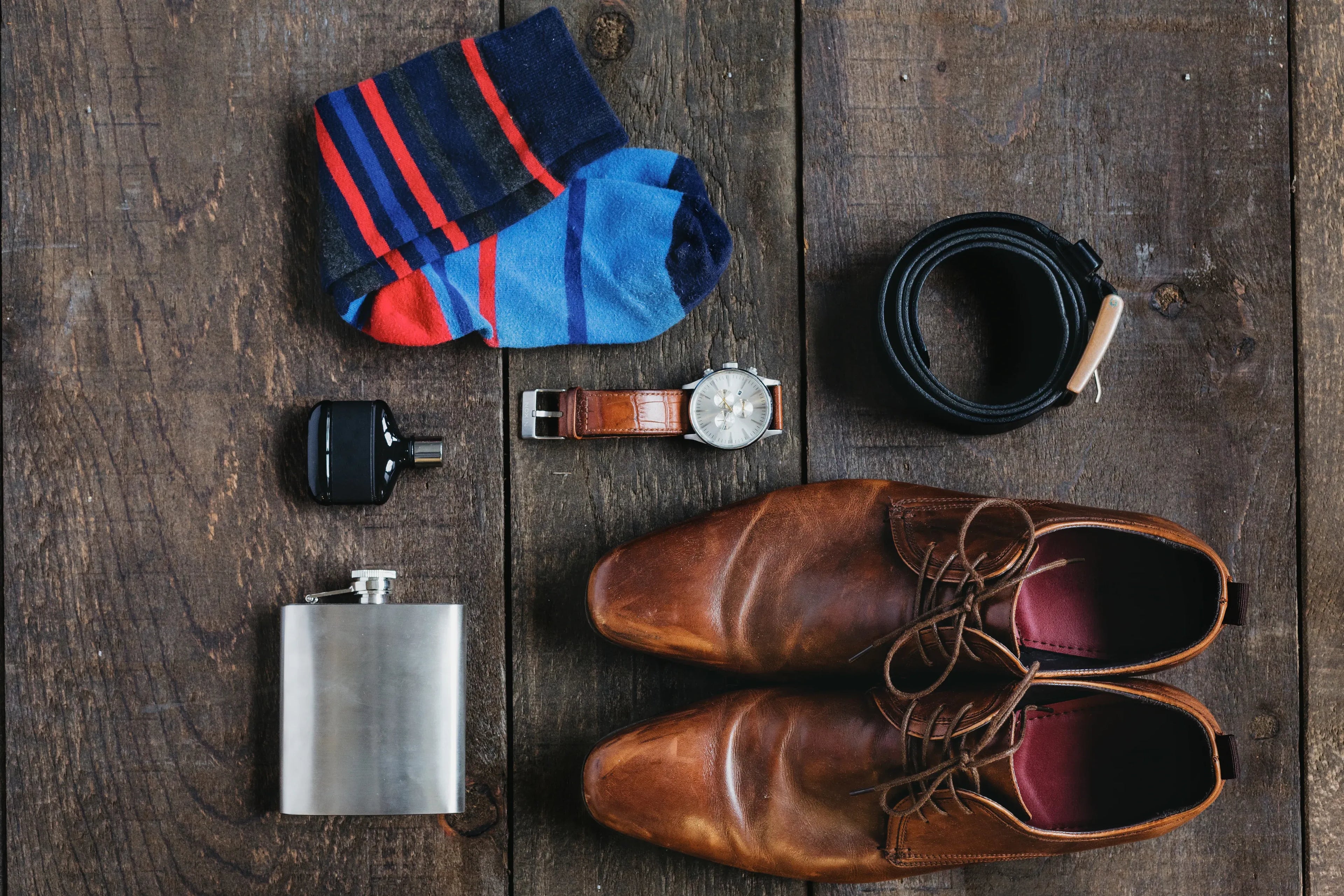 Collection of men's accessories on a wooden surface including shoes, socks, belt, and watch.