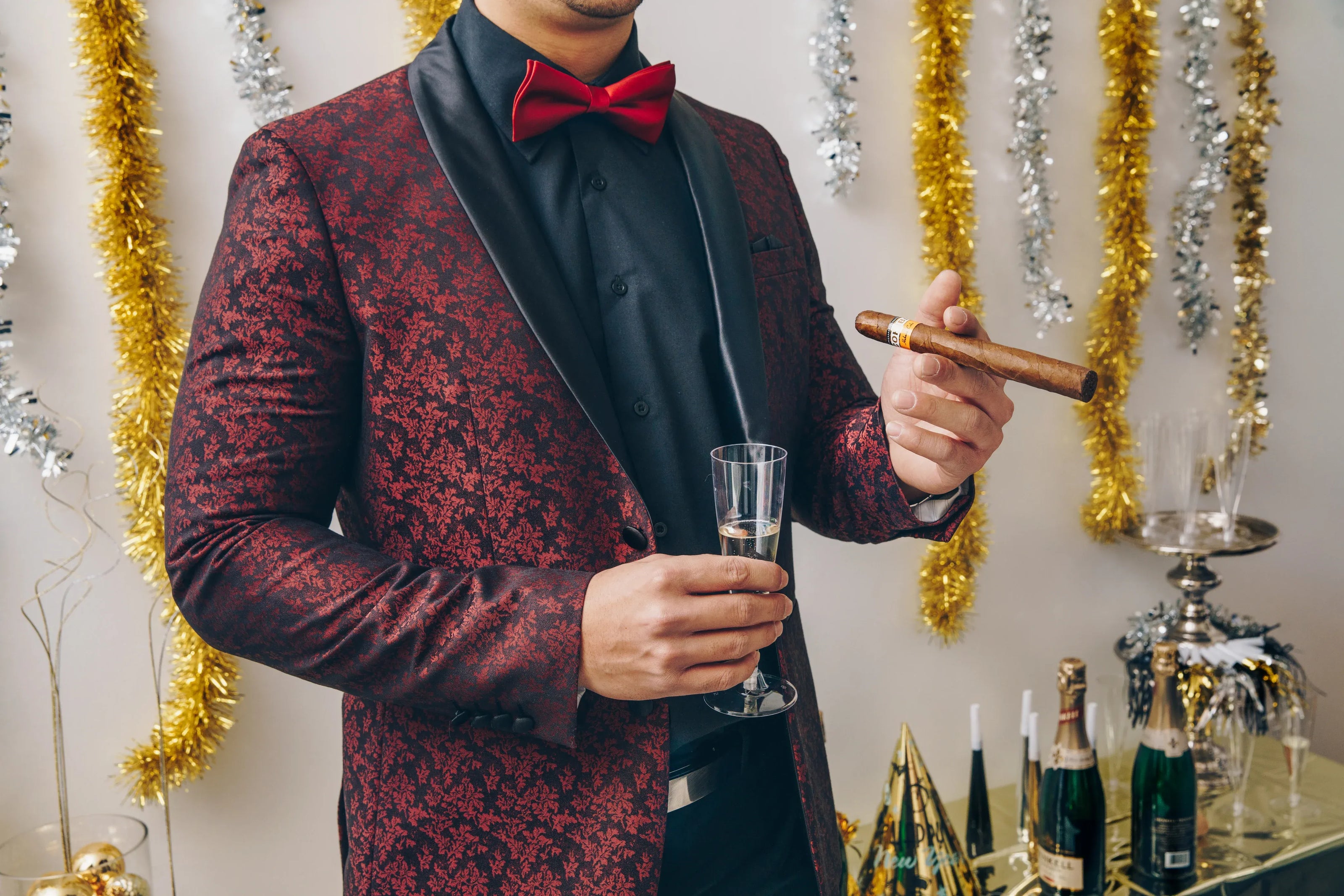 Man in formal attire holding a cigar and glass in a festive setting.